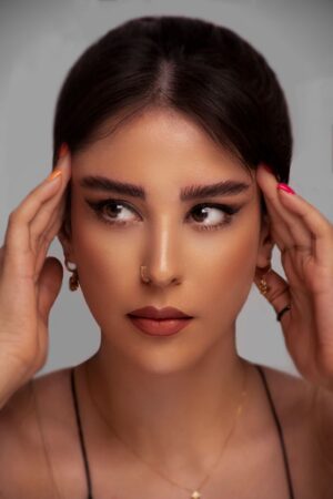 Elegant studio portrait of a woman with brunette hair and subtle makeup on a gray background.
